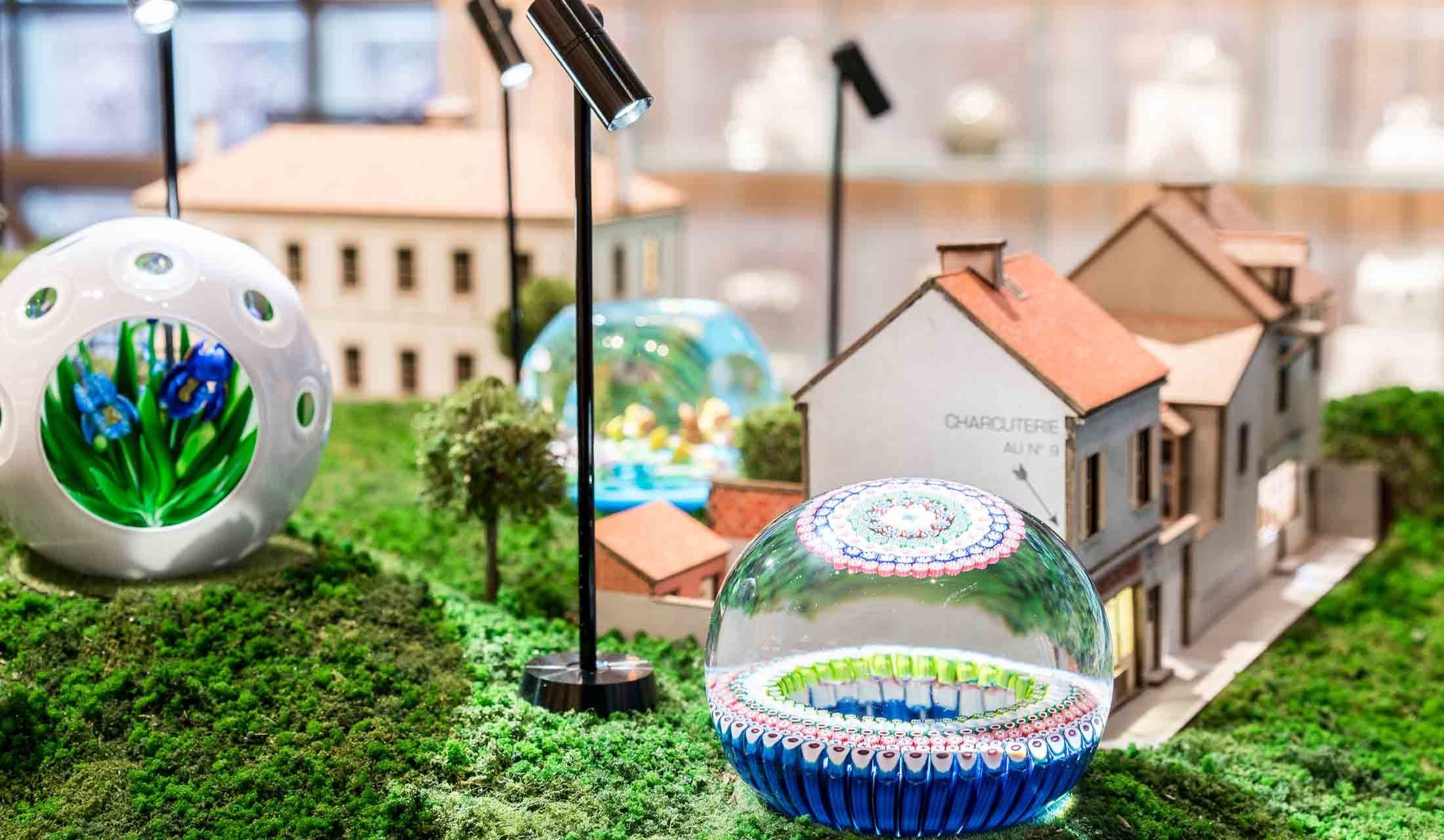 サンルイ村の風景の中にとけこんだクリスタルのペーパーウェイト。右手前が「オーロラ」で、左は「アイリスのブーケ」。2つの大きな窓と10の小さな窓から、華やかなアイリスのブーケを覗くことができる。