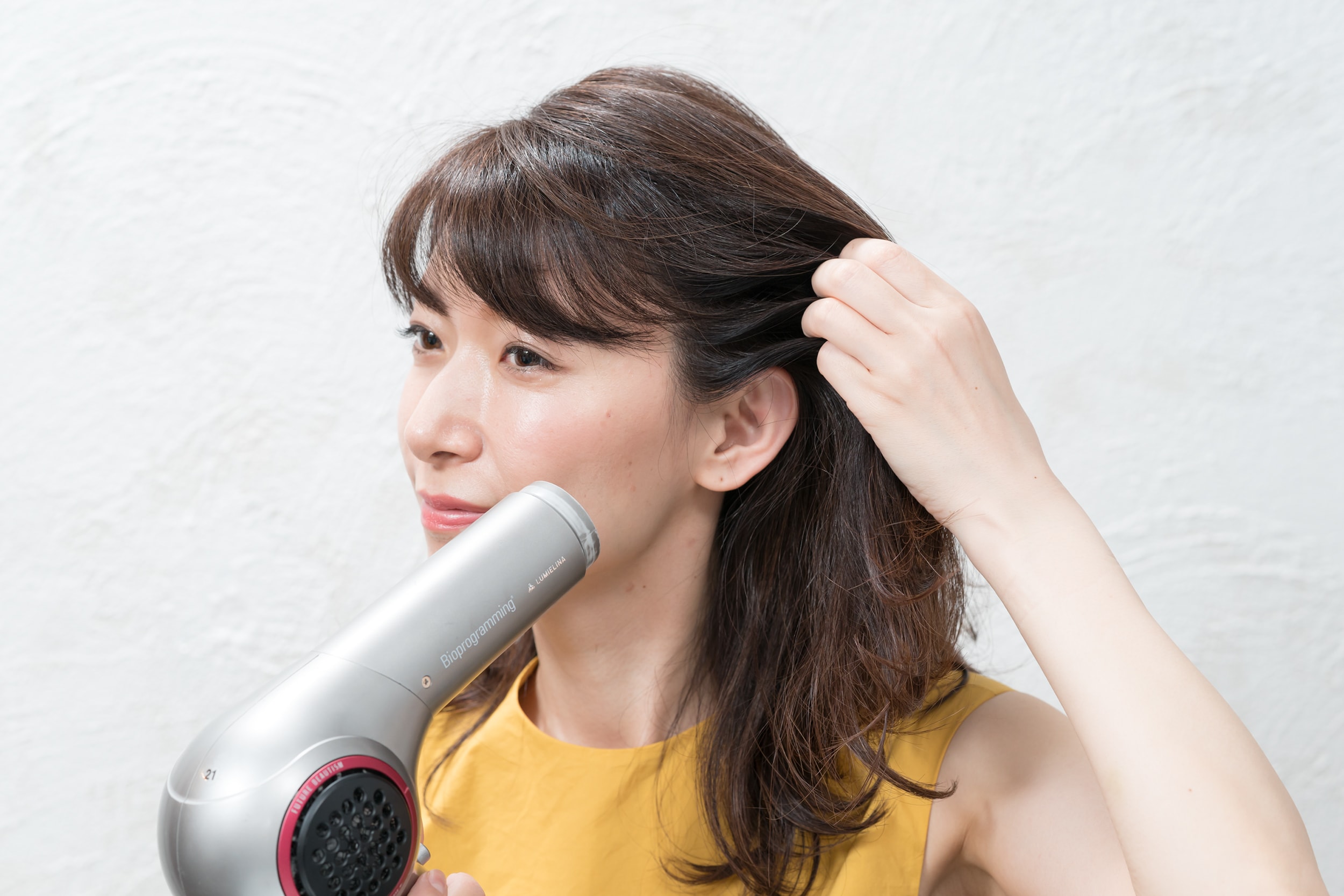 こめかみの髪を後ろに引っ張りながら根元にドライヤーを当ててクセ付ける。