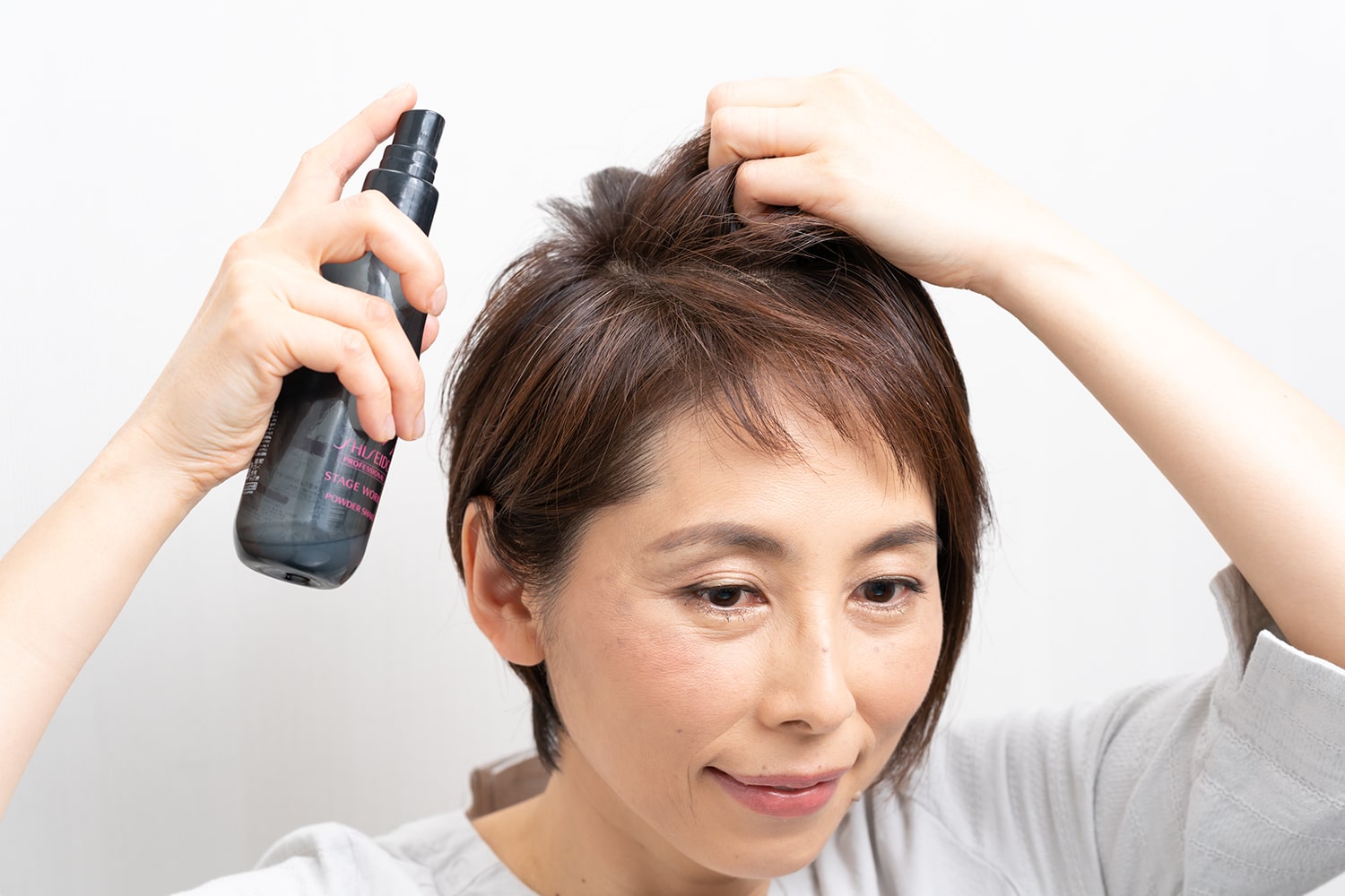 指で髪の根元を握りながらスプレーし、分け目の立ち上がりをキープ。