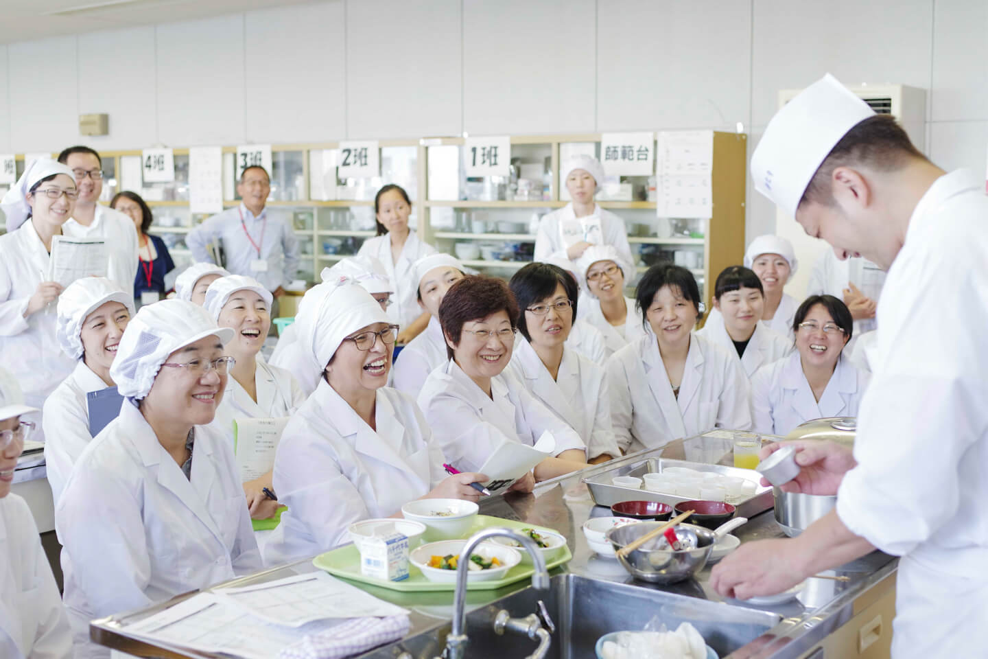 家庭科室にて、和食料理人の実践を白衣を着た栄養士・調理師10名以上が笑顔で見ている