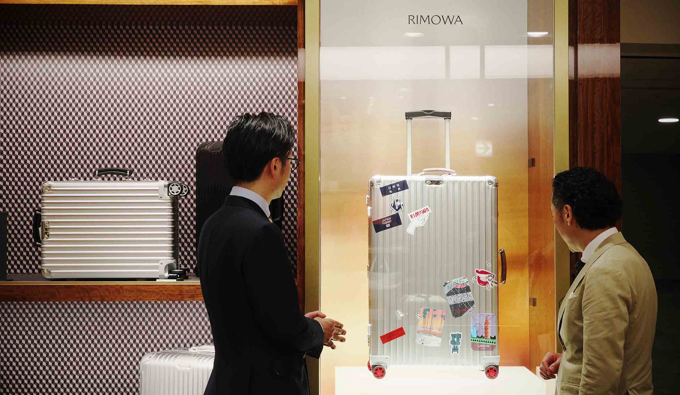 “リモワ”は豊富な品揃えに加え、カスタマイズの楽しみをエスコートするサービスに力を入れている。三越伊勢丹バッグ&ラゲッジのMD、青戸裕明氏(左・トップ画像も)の案内で、旅のイメージを膨らませる矢部。