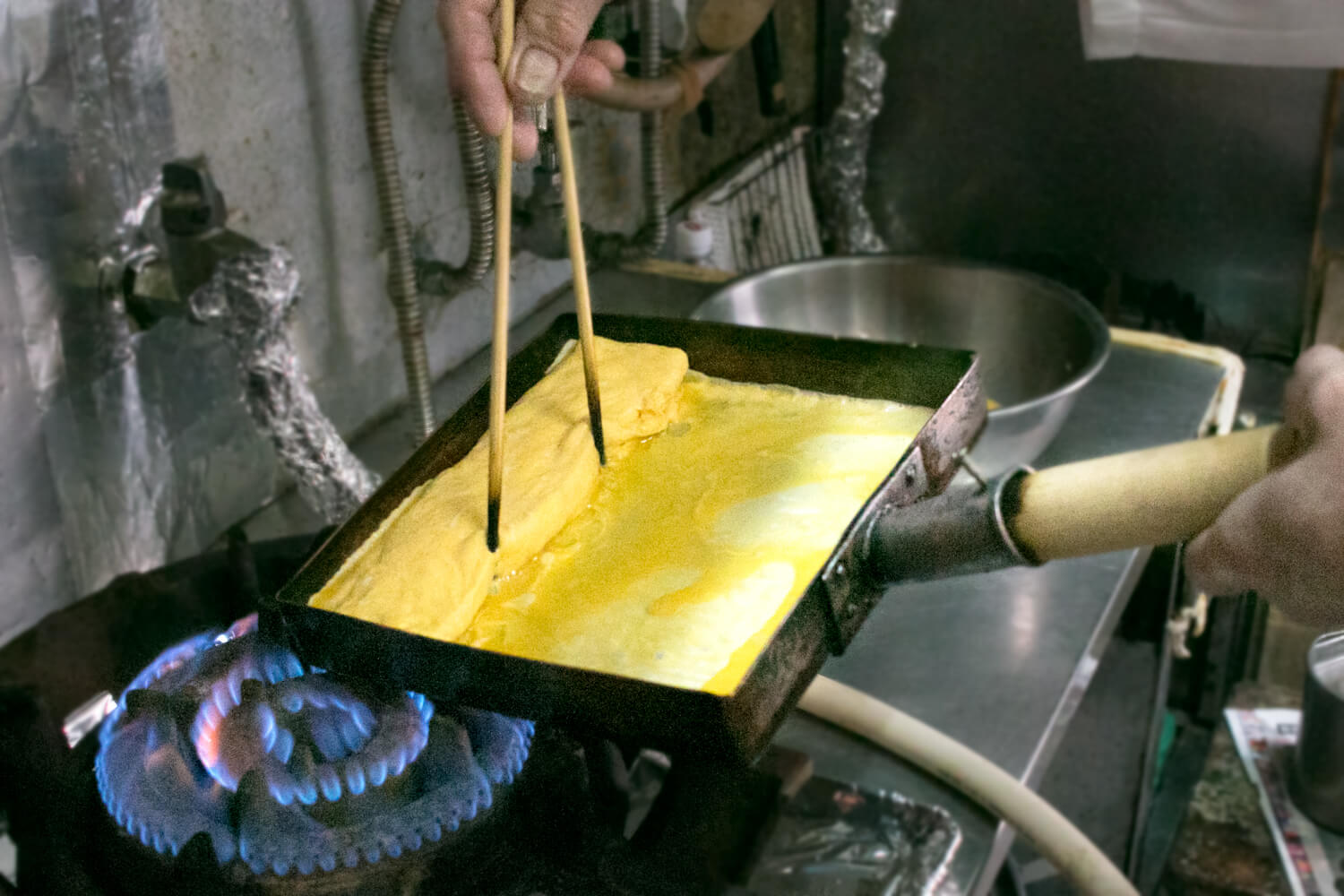 菜箸で玉子焼きを押さえながら玉子焼き器を回すと、形が崩れません