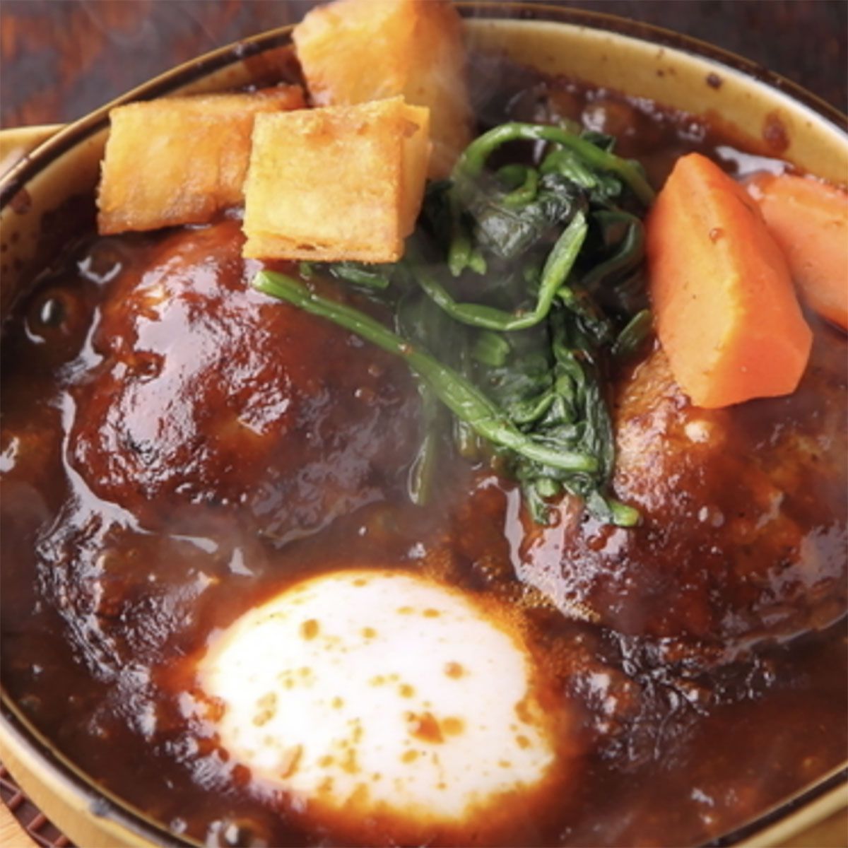 アツアツ、とろとろ『煮込みハンバーグ』(温泉卵のせ)プクプク亭特製のデミソースで煮込んだ、やわらかハンバーグにとろとろの温泉卵を絡めていただく逸品です。